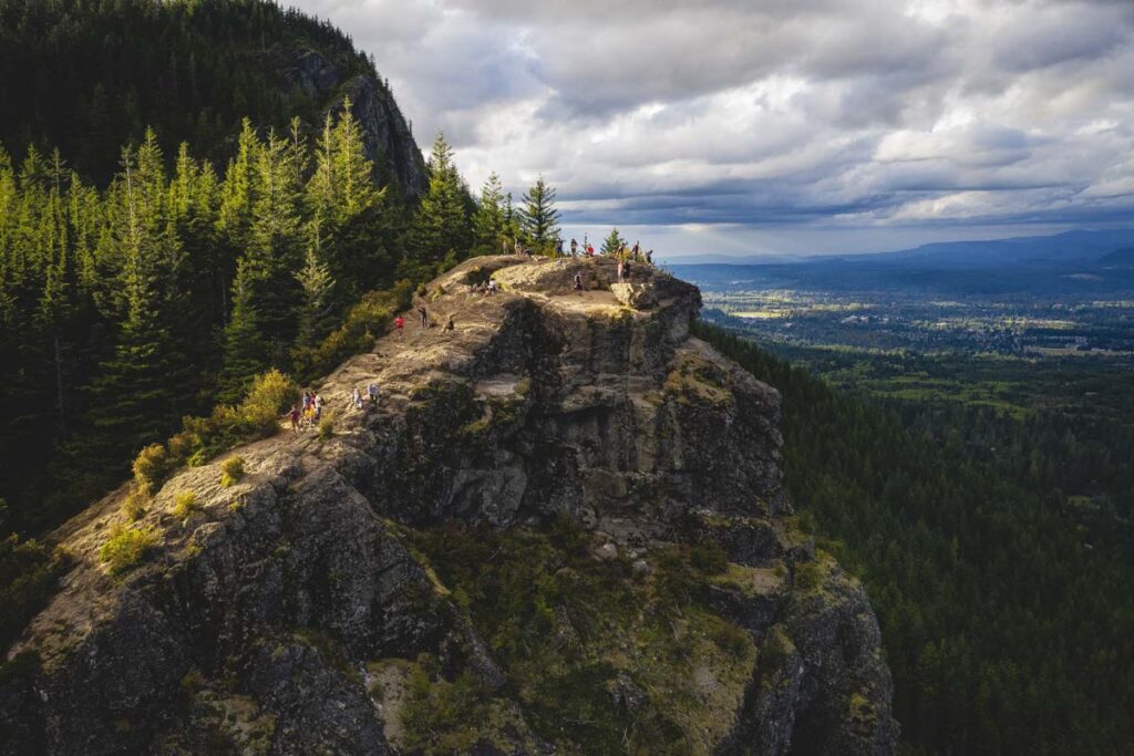 Groups of people hiking up Rattlesnake Ledge Trail to the summit with a great view across the valley on an overcast day.