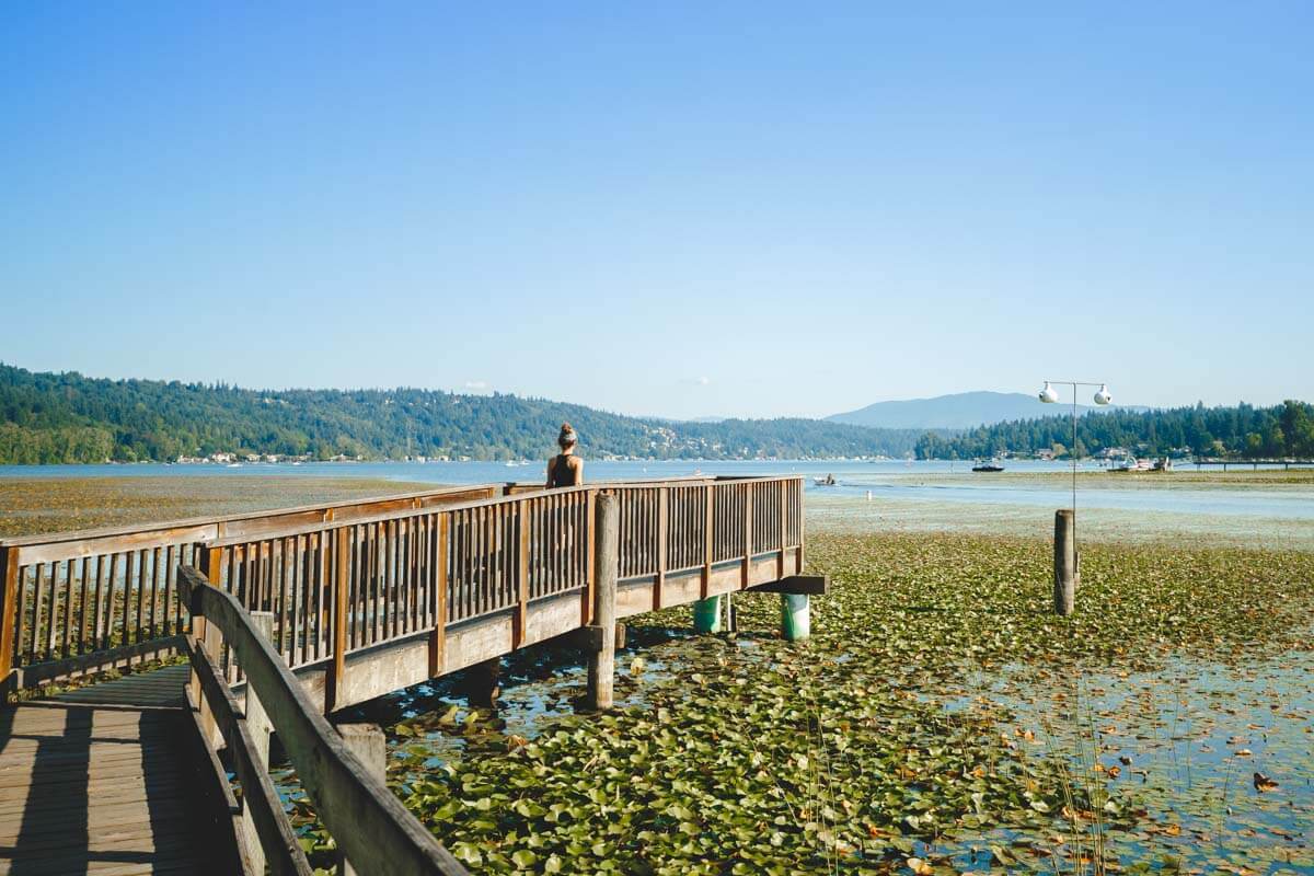 Nina walking along a wooden jetty out over Lake Sammamish with lily pads covering the water.