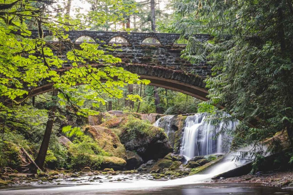 A historic stone bridge crossing Whatcom Falls near Bellingham with trees and rocks surrounding it.