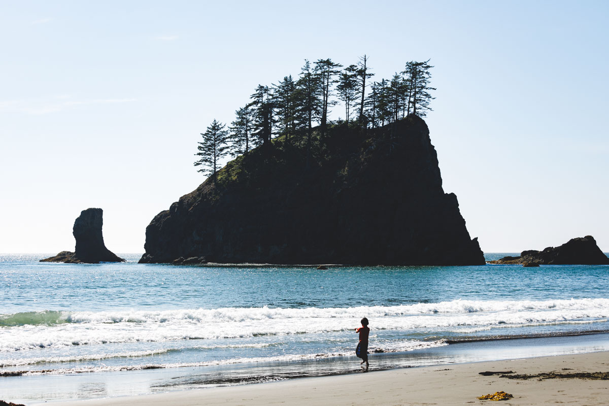 A small child playing on La Push Second Beach with a view of an island out in the ocean.