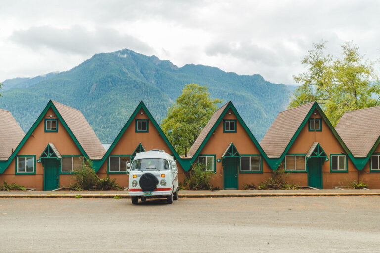 Lucy, our VW Bus parked outside of cute A frame cabins in Olympic National Park with mountains in the back.