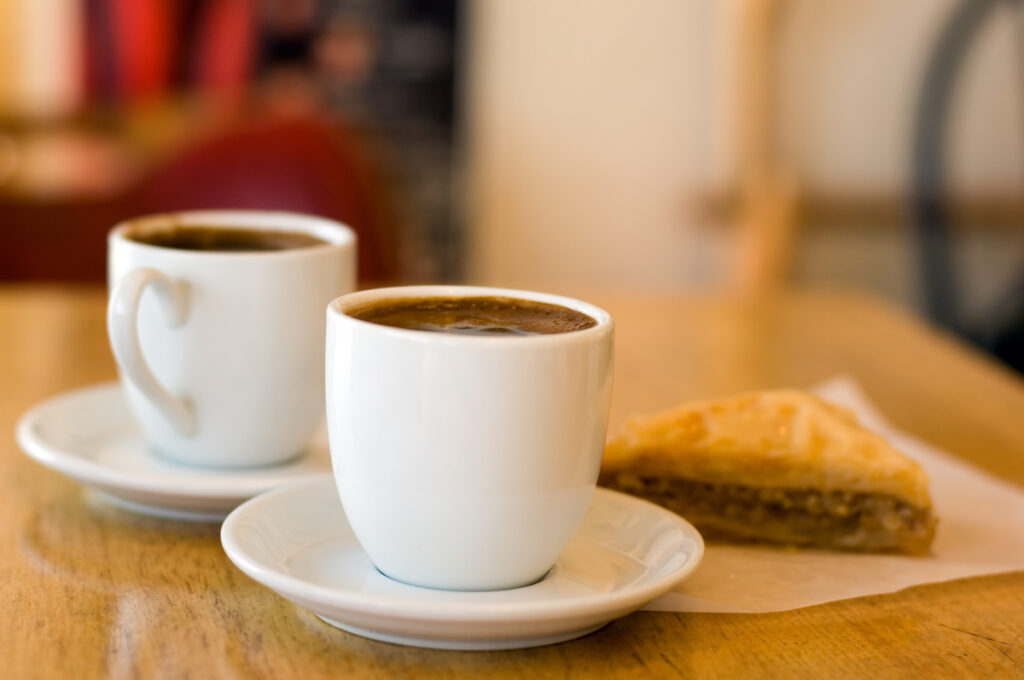 Two cups of coffee in white mugs on a cafe table besides a pastry treat.