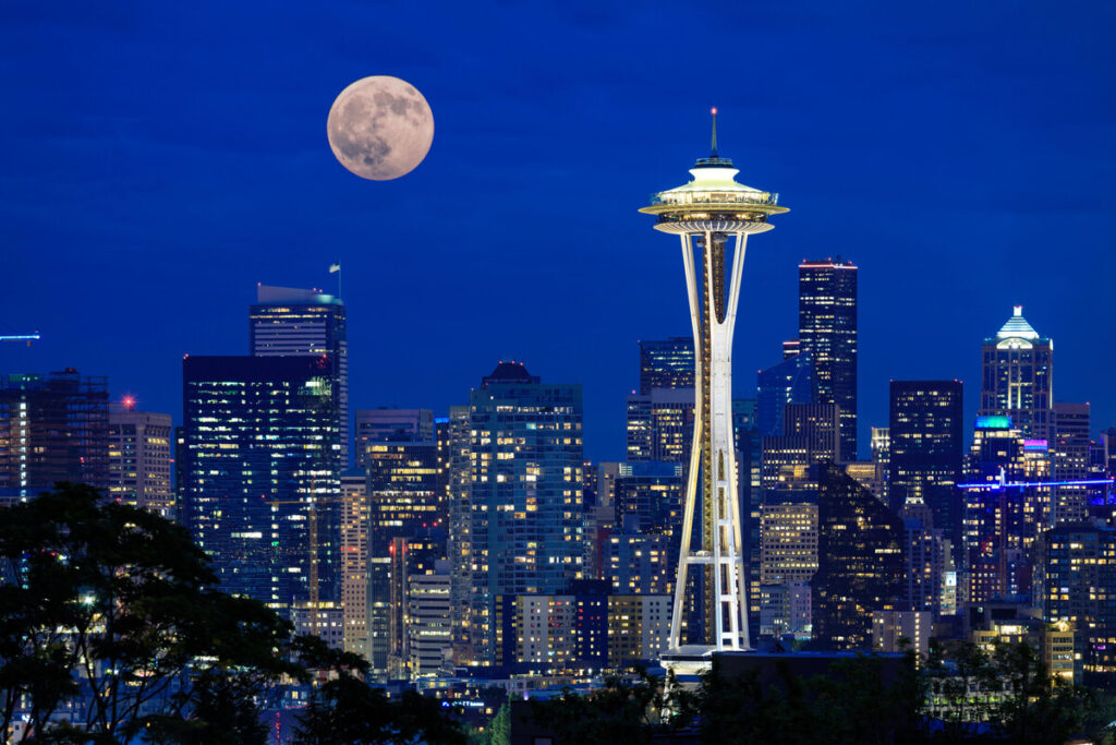 Seattles skyline and the Space Needle at night with the full moon over the city.