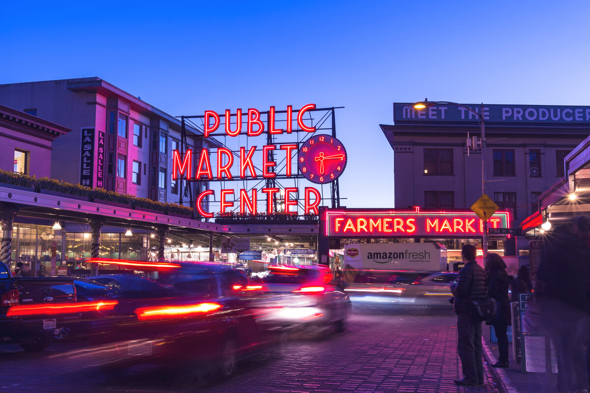 A bright red neon sign at the entrance of Pike Place farmers market while cars pass outside.