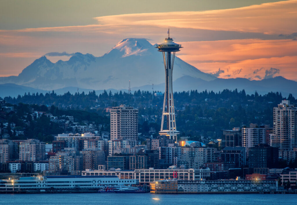 A stunning view of the Space Needle in downtown Seattle with a backdrop of a mountain at sunset.