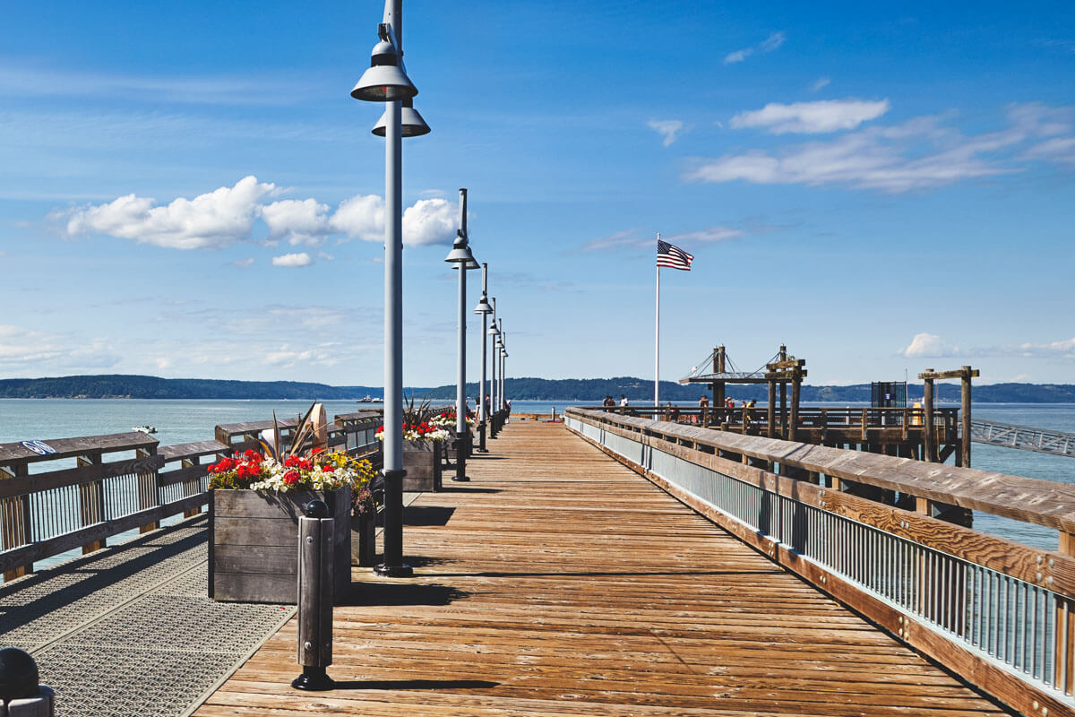 View down the Old Town Dock in Tacoma with lampposts down it's length and an American flag on a pole.