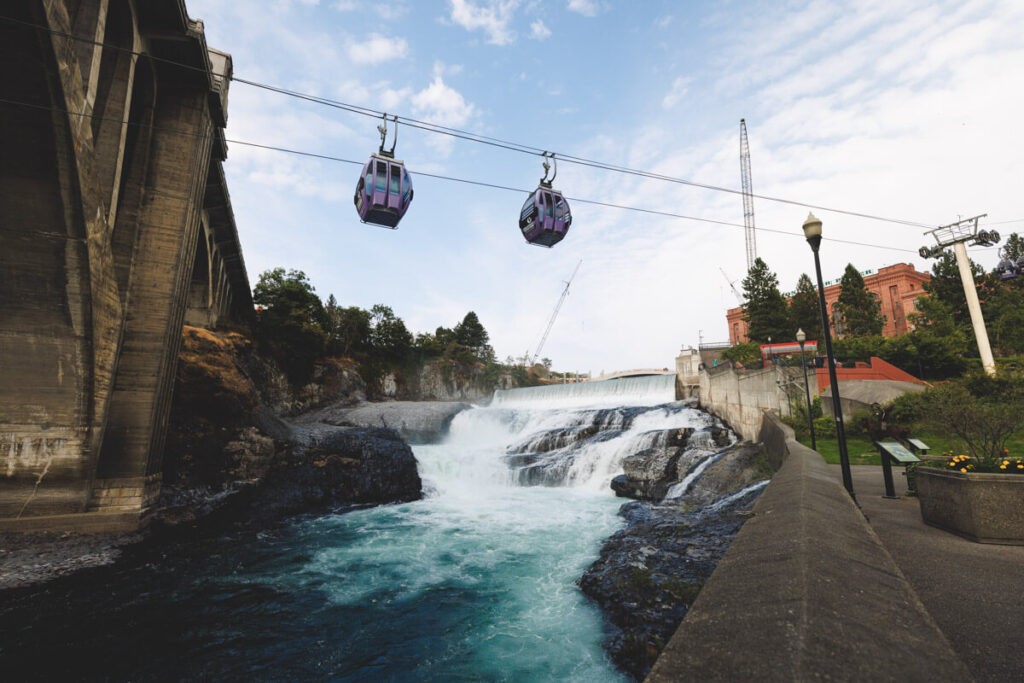 Two gondolas crossing over a river and waterfall in Riverfront Park in Spokane.