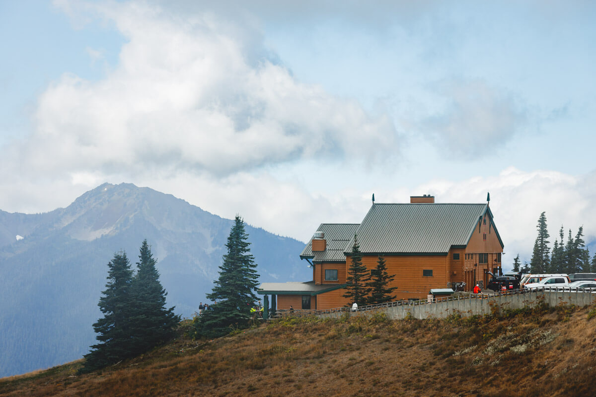 The large orange-colored Hurricane Ridge Visitor Center perched on the edge if a hill with a mountain view.