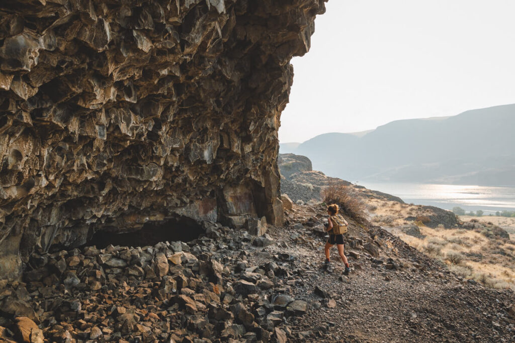 A woman hiking pass a small cave along the Lake Lenore Caves Trail.