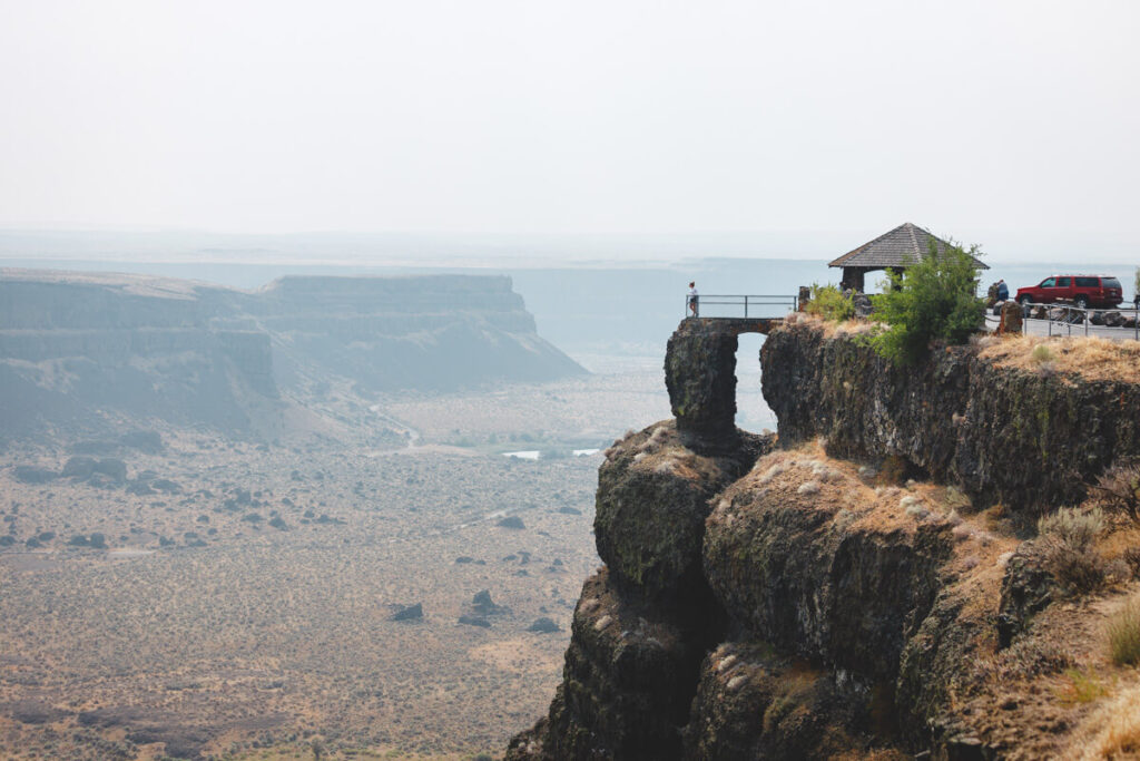 A woman standing on a cliffside viewpoint overlooking Dry Falls State Park.