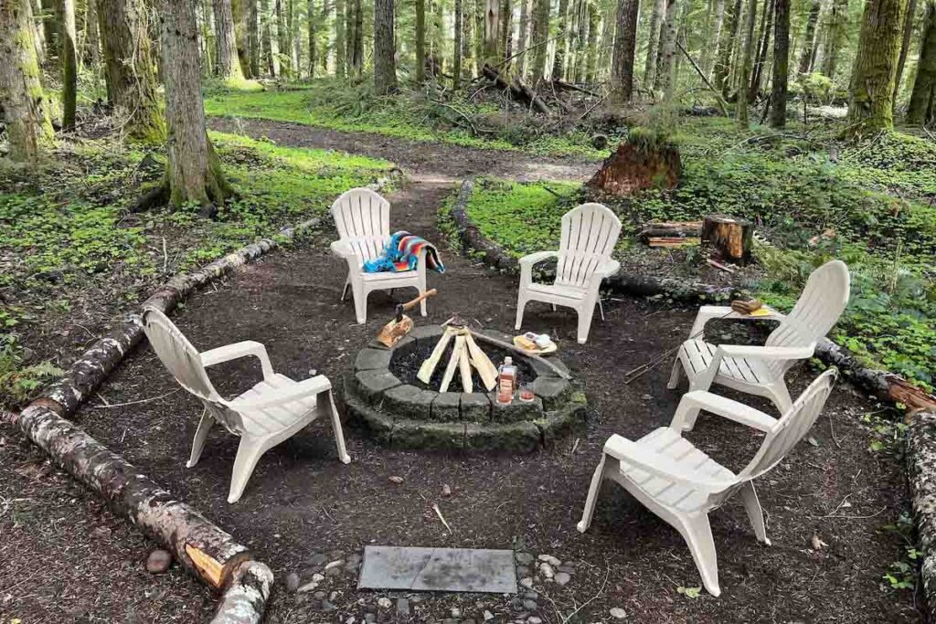 A circle of garden chairs surrounding a fire pit in the forest.