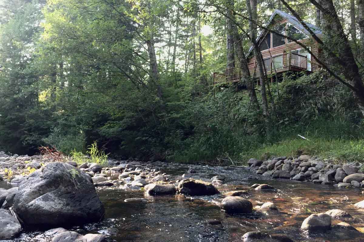A view of a cabin from the creek down below in the middle of the forest in Washington.