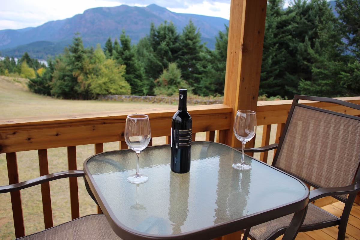 A bottle of red wine and two glasses on the balcony table of Shellrock Cabin with a view over Columbia River Gorge.