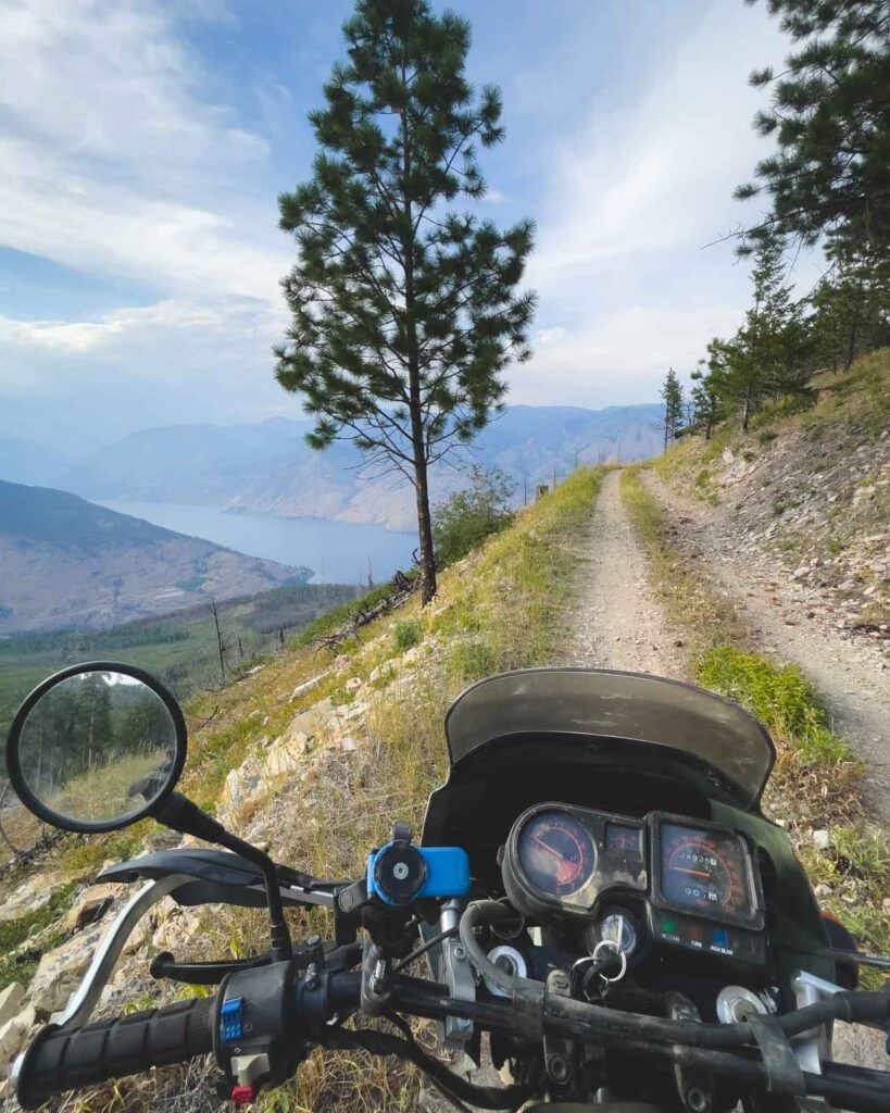 Motorcycle cockpit view while riding down the dirt trails with a backdrop of Lake Chelan.