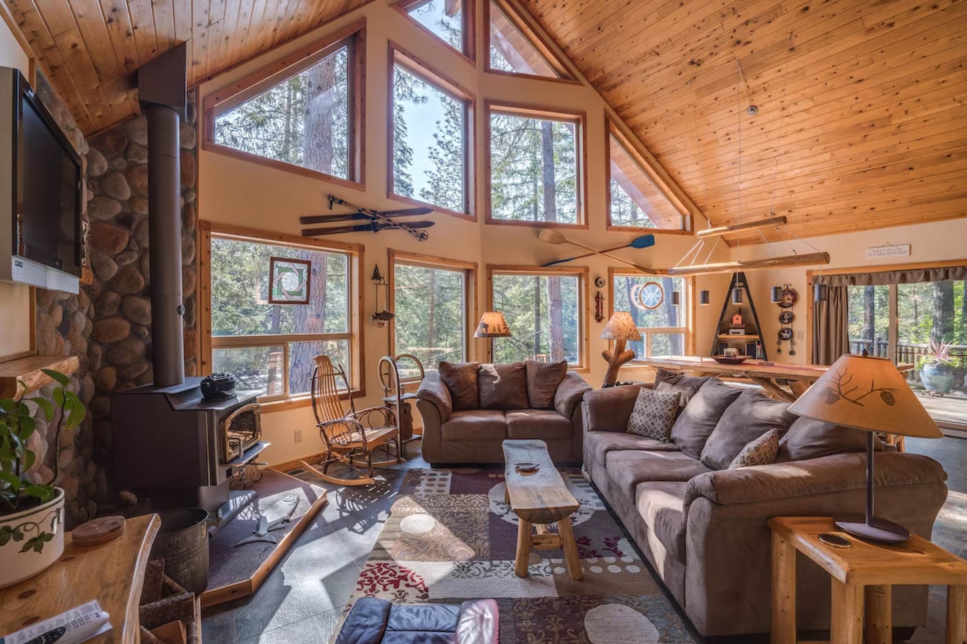 Two comfy looking sofas and a wood burner and chimney inside the living area of a wooden cabin with giant windows looking into the forest.