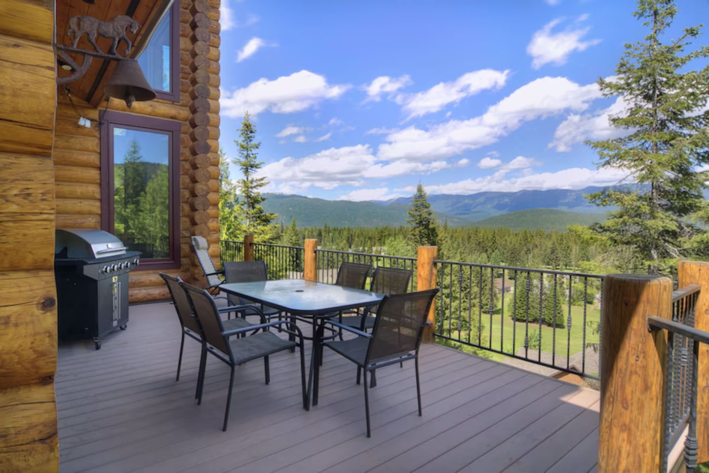 A gas BBQ and patio furniture on the decking of the Lux Lodge with a view over the forest on a sunny day.