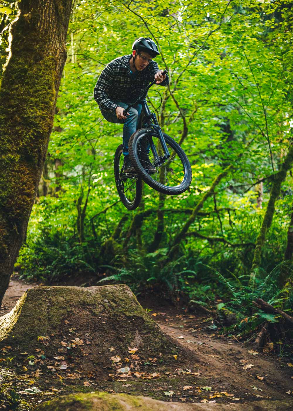 A man on a mountain bike in mid-air after jumping off a dirt jump int he middle of the forest.