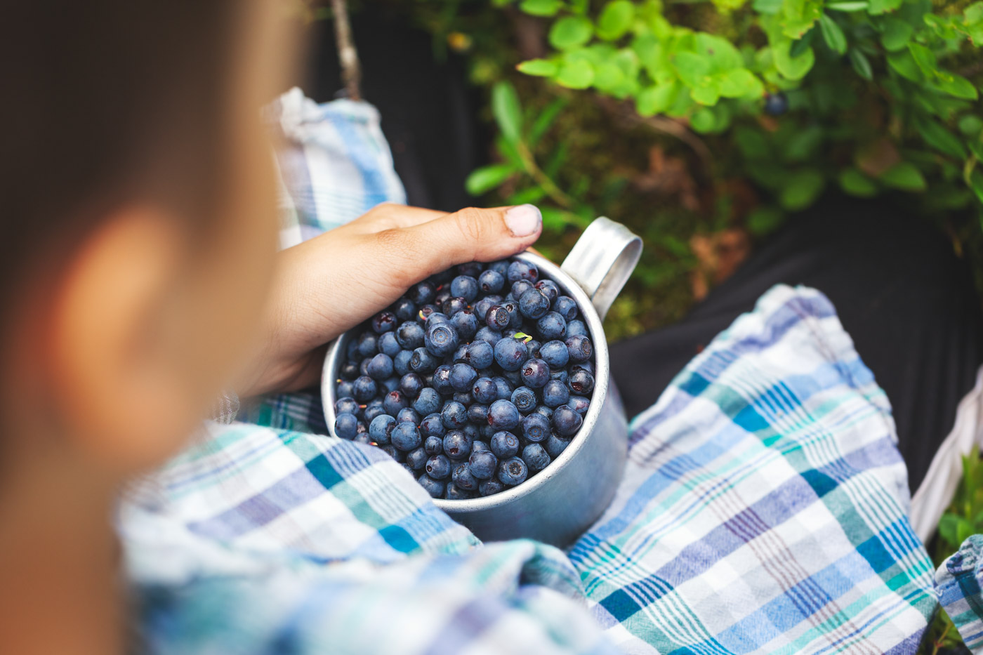 A small boy holding a metal mug full of blueberries.