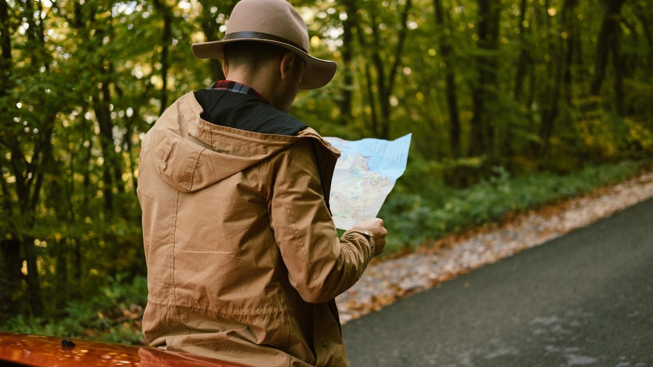 Traveler man with hat looking map near car in autumn forest