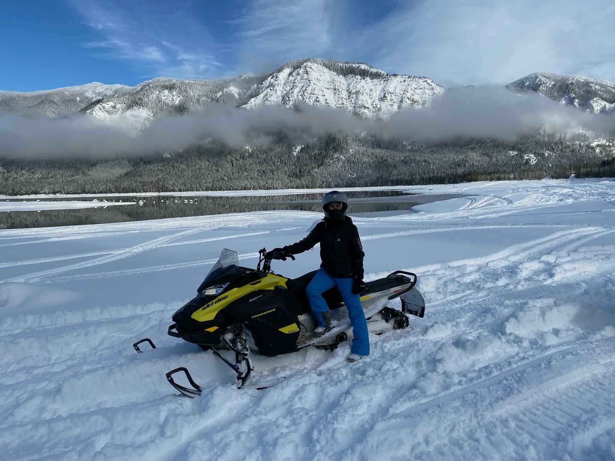 Woman snowmobile with mountain backdrop.